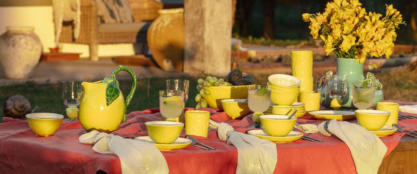 Sunny outdoor table setting with yellow Bordallo Pinheiro ceramic tableware, a lemon-shaped jug and fresh flowers