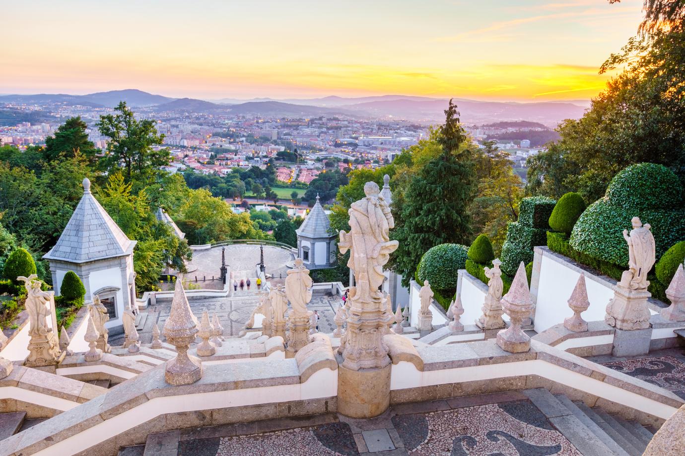 Sunset view over Braga from the top of the Bom Jesus do Monte staircase with baroque statues in the foreground