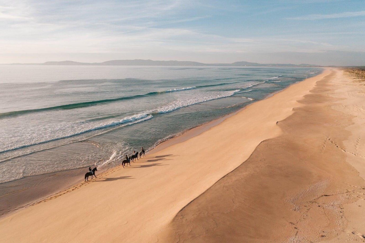 Aerial view of horseback riders on the beach at sunset near Comporta, Portugal, run by Cavalos na Areia