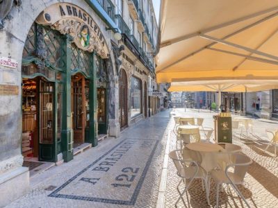 Hero A Brasileira Street The green and gilded entrance of A Brasileira café on Rua Garrett in Chiado, Lisbon, with a mosaic pavement and terrace tables in the sun