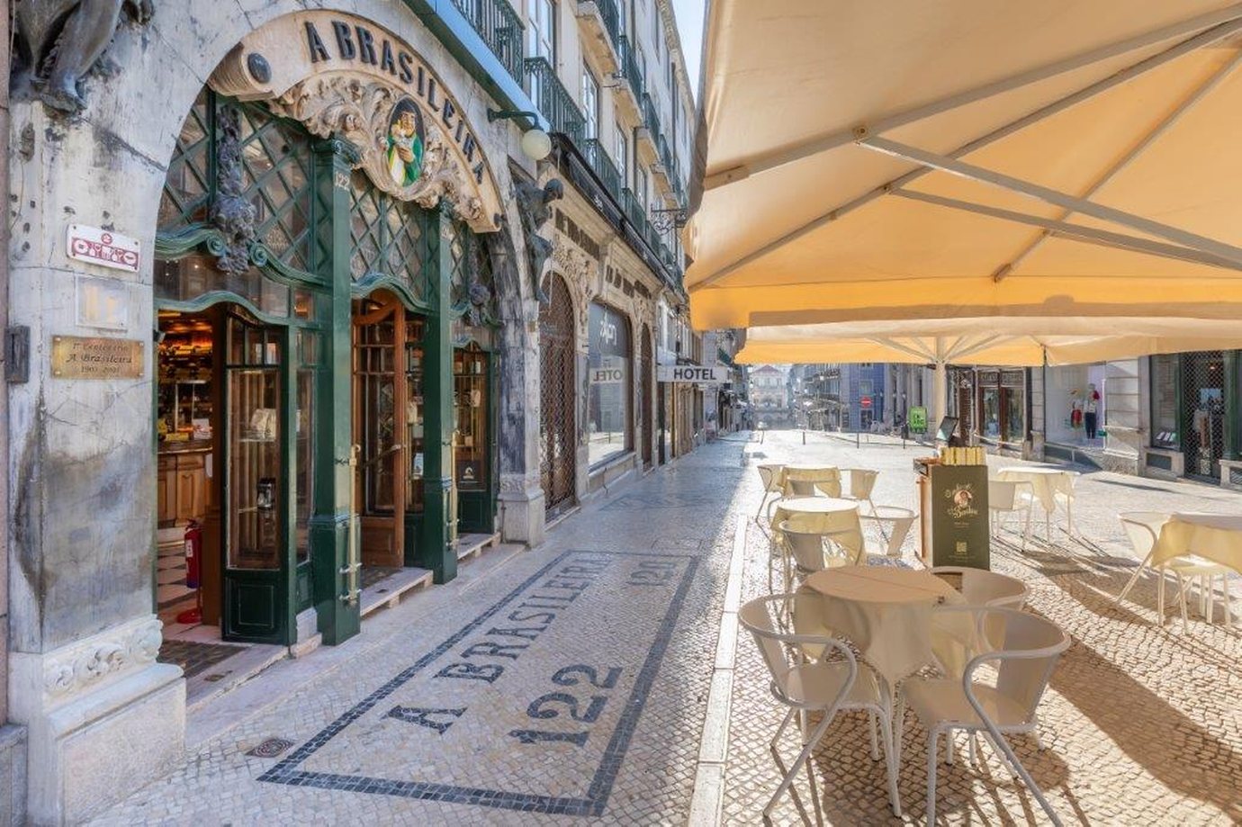 The green and gilded entrance of A Brasileira café on Rua Garrett in Chiado, Lisbon, with a mosaic pavement and terrace tables in the sun