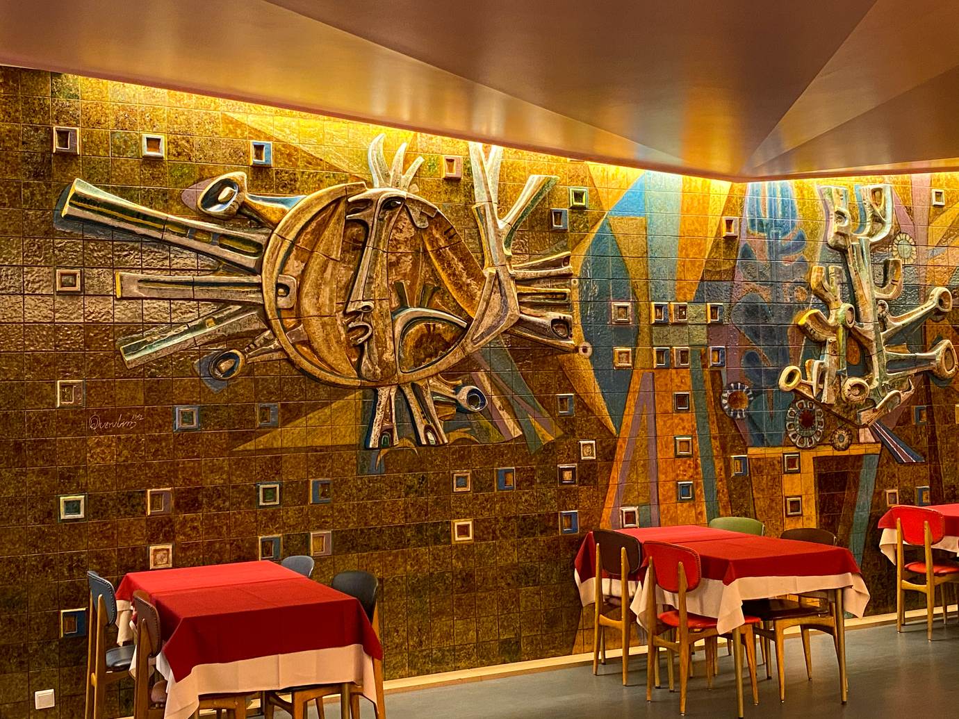 A large 1962 ceramic and metal sun mural in warm gold and orange on the wall of the Pastelaria Mexicana dining room in Lisbon