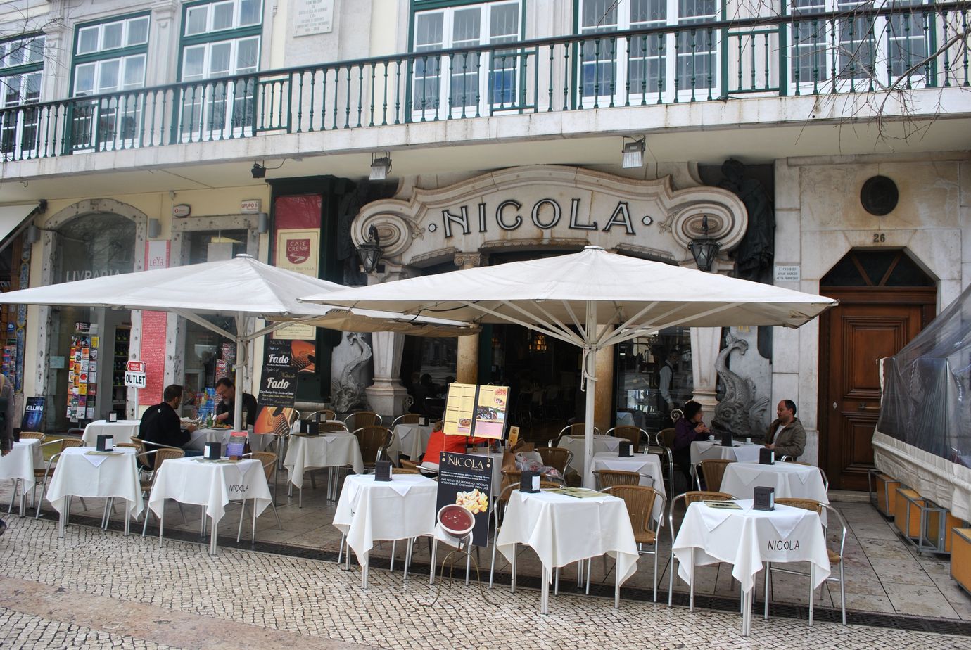 The curved Nicola sign and white-clothed terrace tables under umbrellas at Café Nicola on Rossio Square in Lisbon