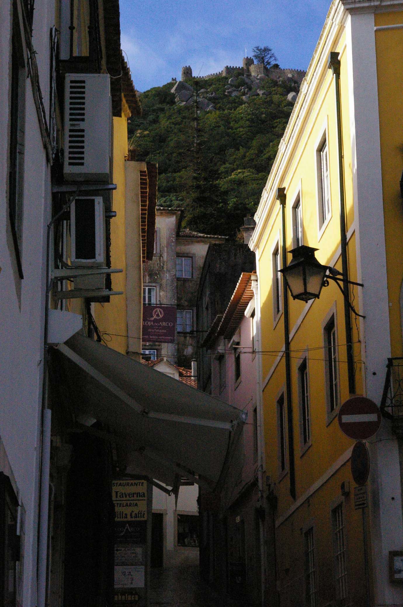 A narrow lane in Sintra’s old town between yellow houses, with wooded hills rising above the rooftops