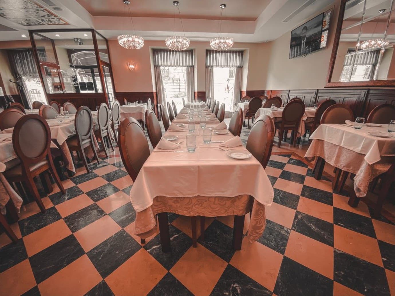 The dining room of Pastelaria Versailles in Lisbon with a long table set under chandeliers and an orange and black chequered marble floor