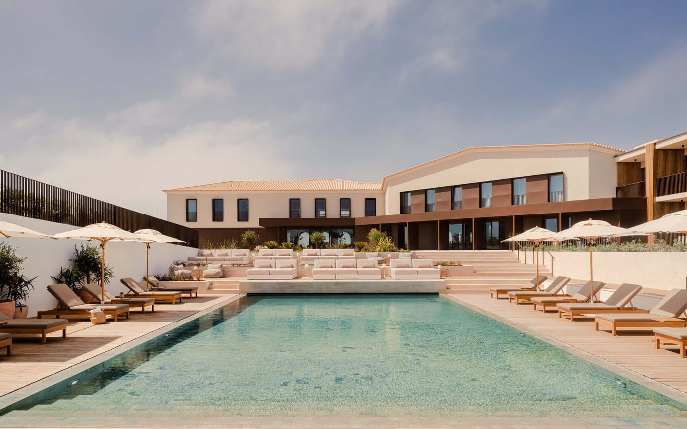The pool terrace of Aethos Ericeira with sun loungers and white umbrellas in front of the low modern hotel building