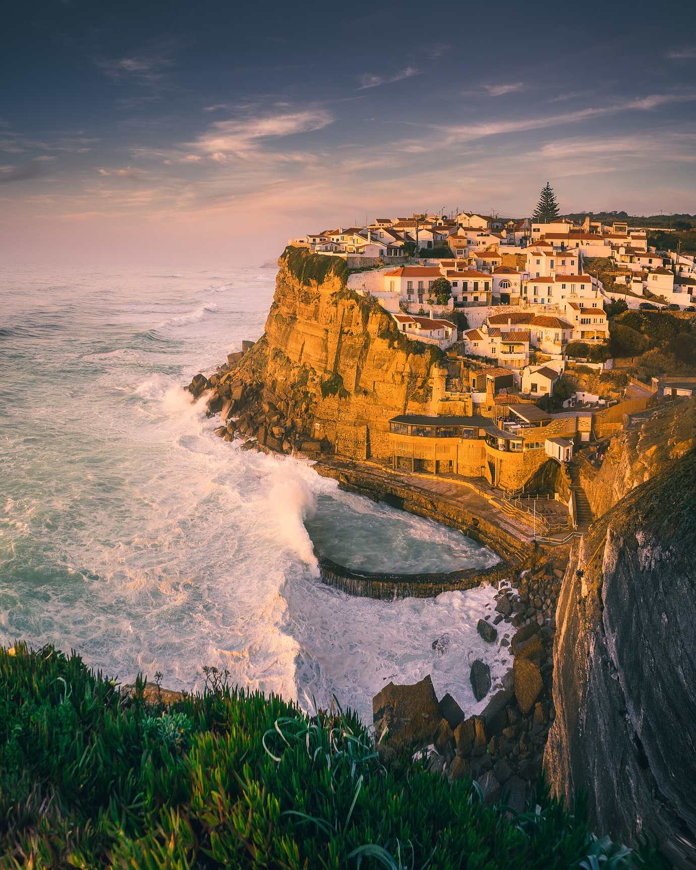 The white village of Azenhas do Mar glowing gold in the evening light on a cliff above breaking waves