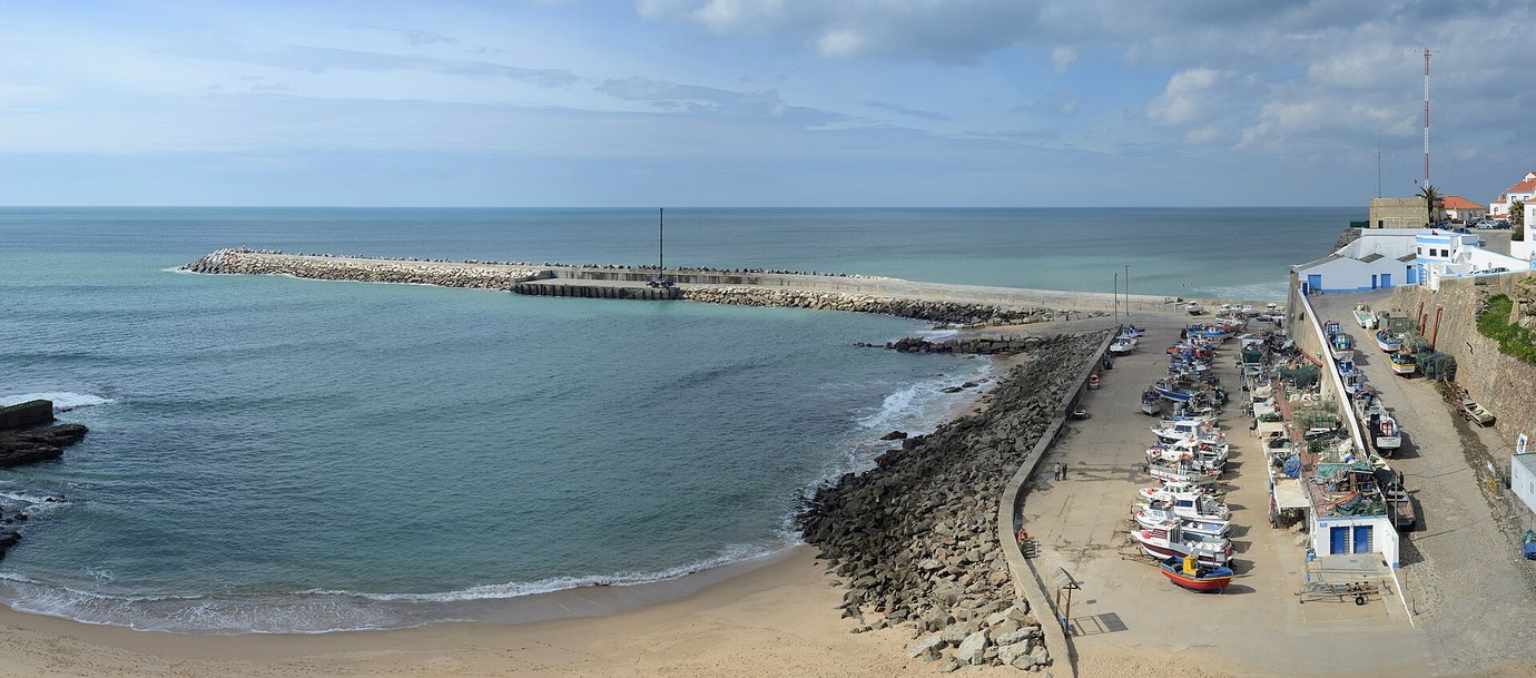 Fishing boats on the slipway beside the harbour wall and the beach at Ericeira, with the town above the cliff on the right