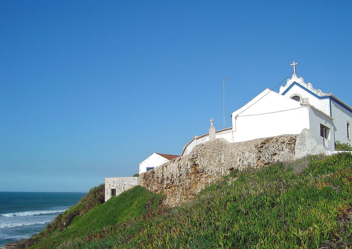 The white chapel of São Julião on a green headland above the sea near Ericeira under a deep blue sky