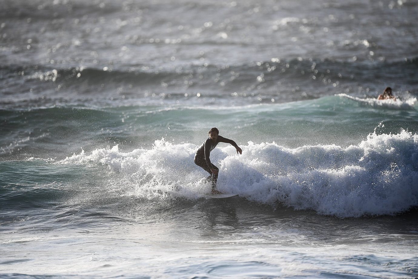 A surfer riding a breaking wave in grey-green water off the coast at Ericeira