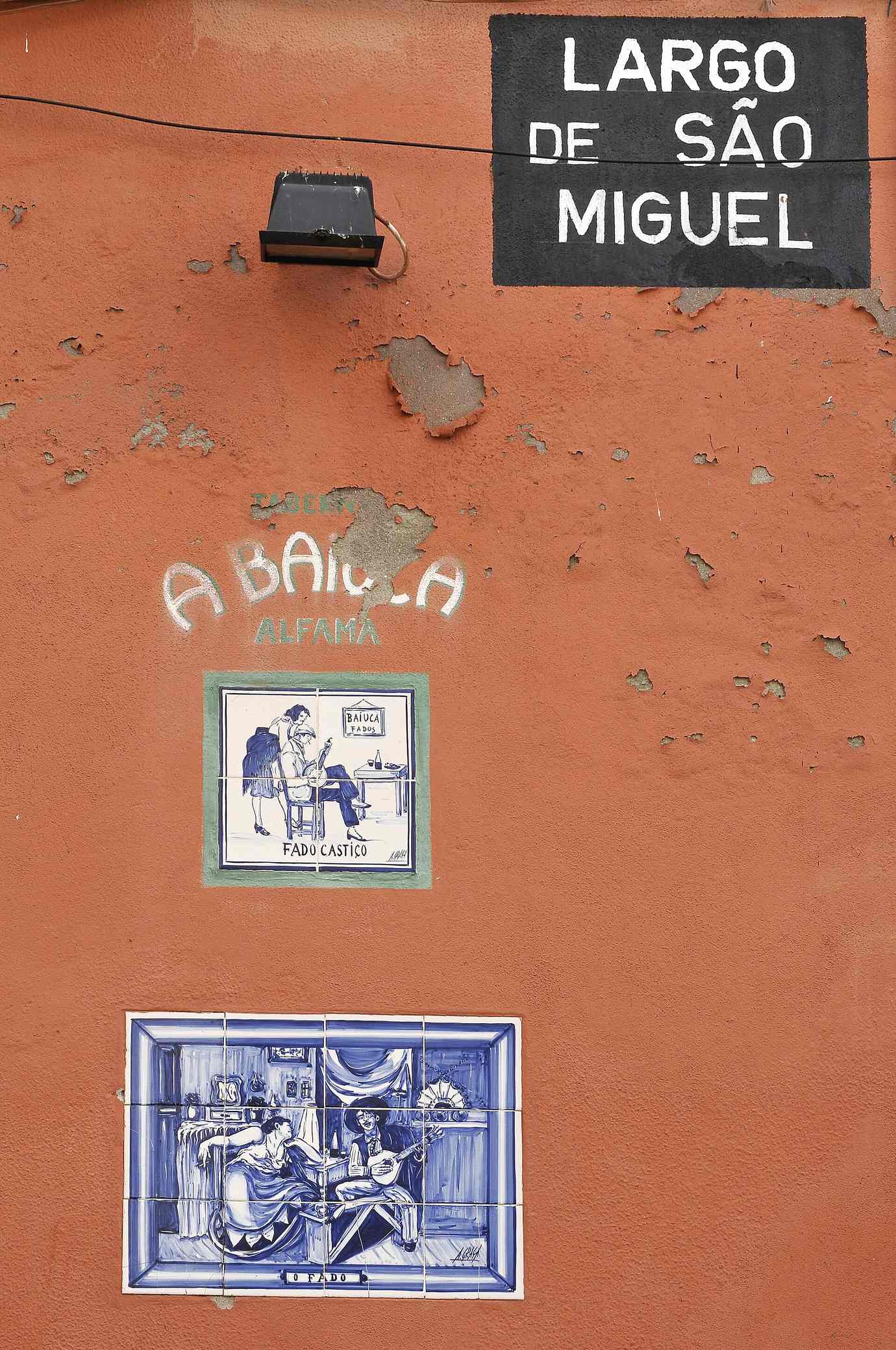 An orange wall on Largo de São Miguel with the hand-painted name A Baiuca Alfama above two blue and white fado azulejo plaques