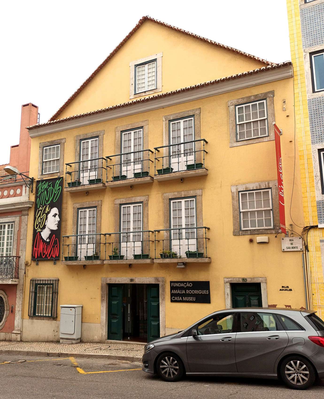 The yellow façade of the Amália Rodrigues house museum on Rua de São Bento in Lisbon, with a banner showing the singer