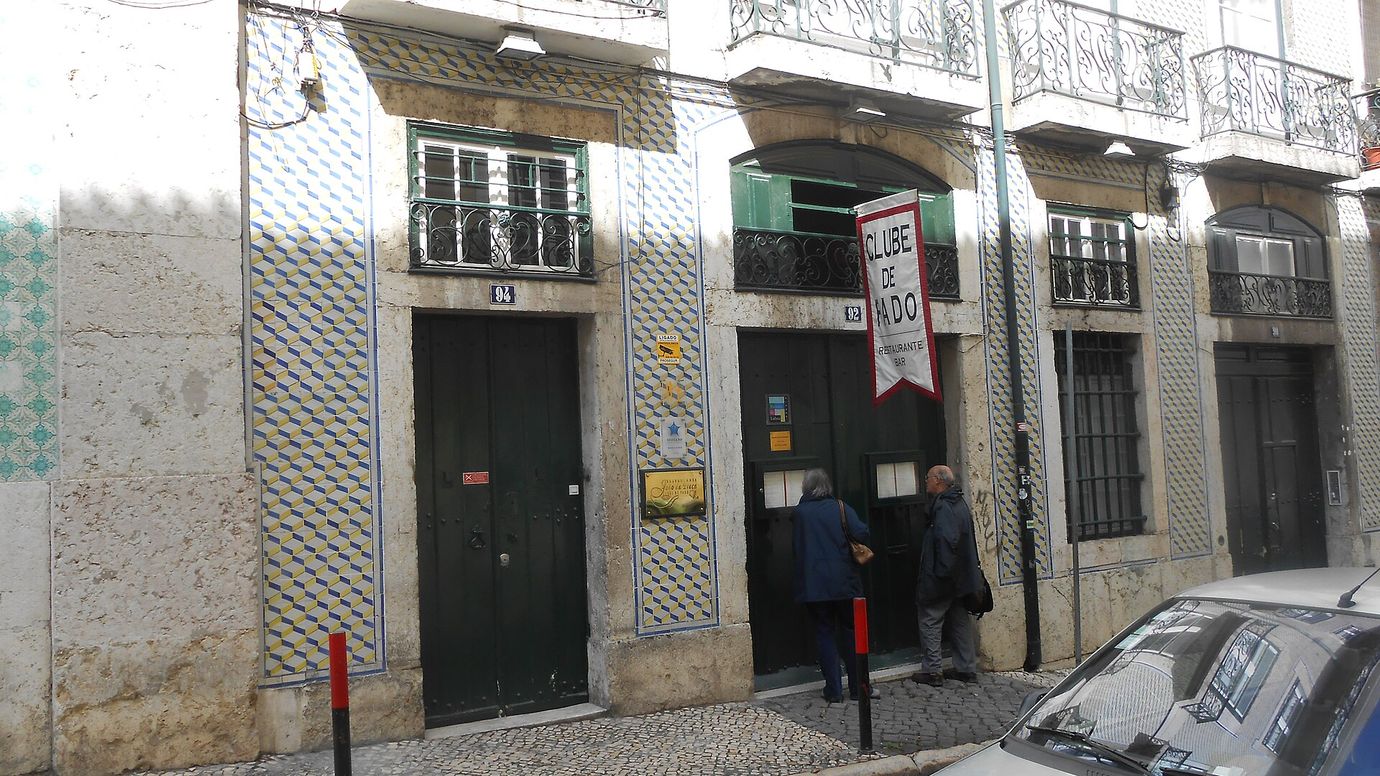 The tiled street front of the Clube de Fado in Alfama with a red banner and dark green doors