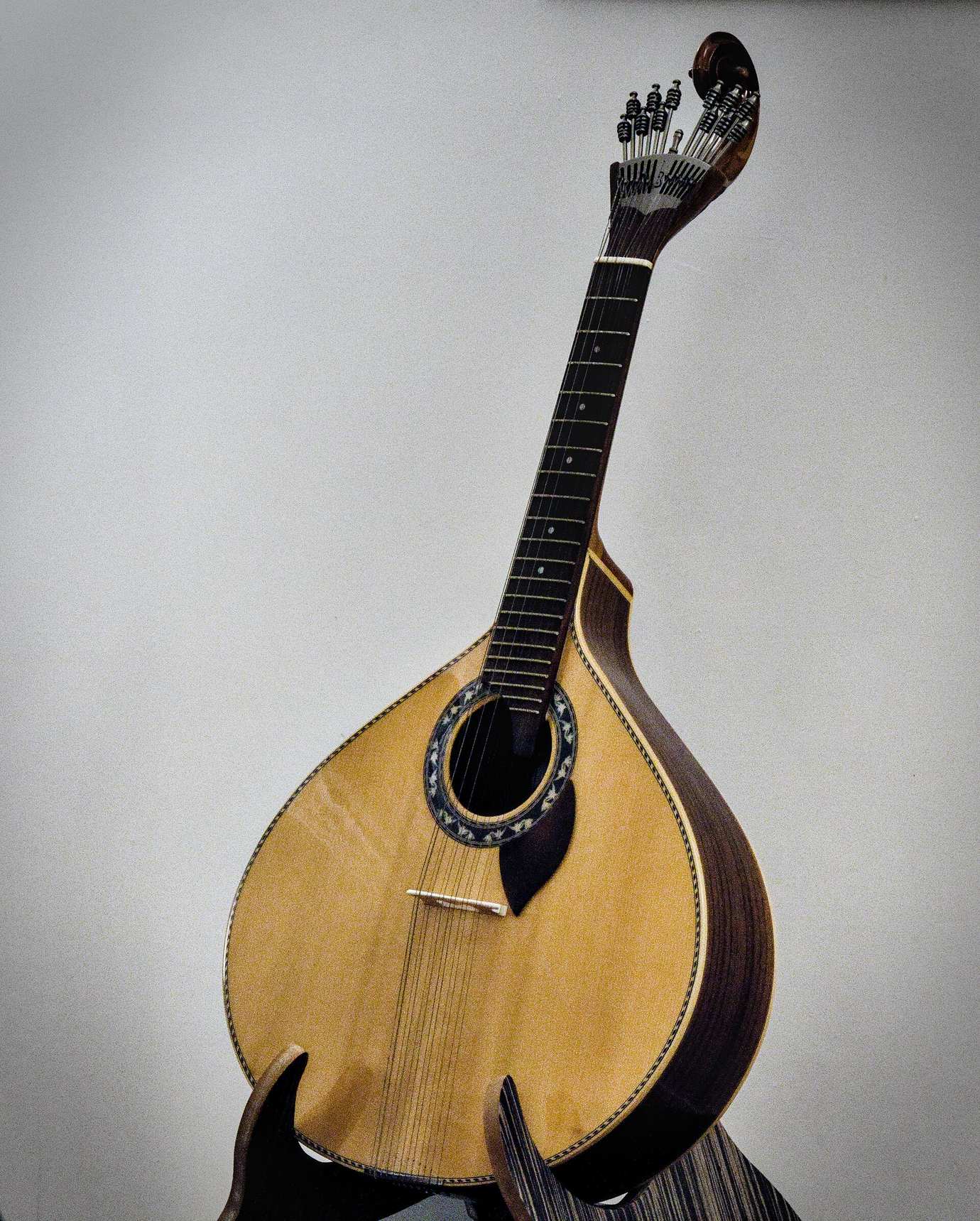 A Portuguese guitar with its teardrop-shaped wooden body and twelve tuning pegs on a pale grey background