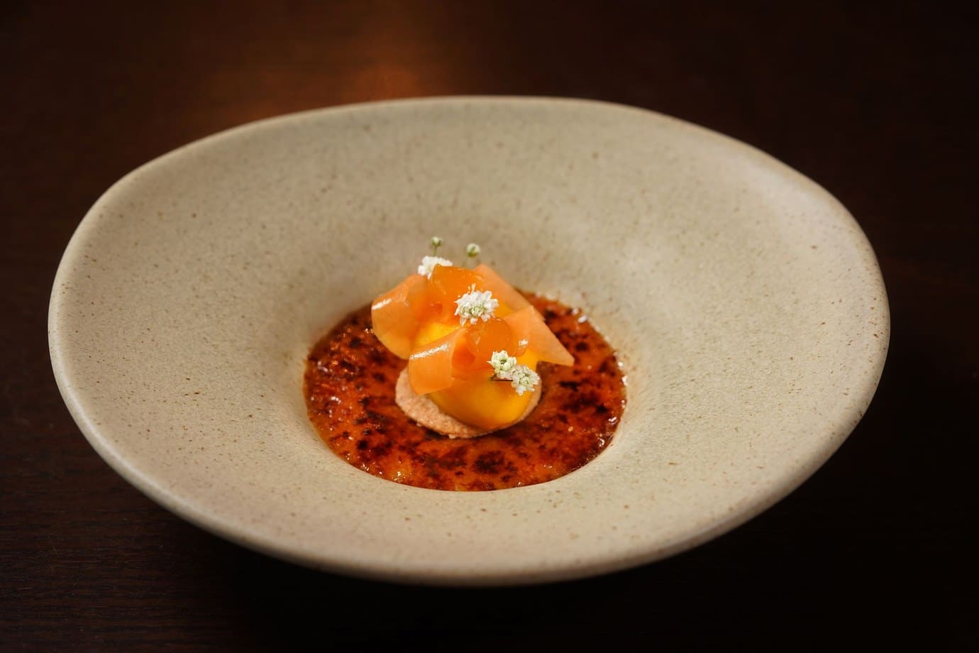 A dish of orange and red ingredients with edible flowers served in a pale stoneware bowl at the restaurant A Cozinha in Guimarães