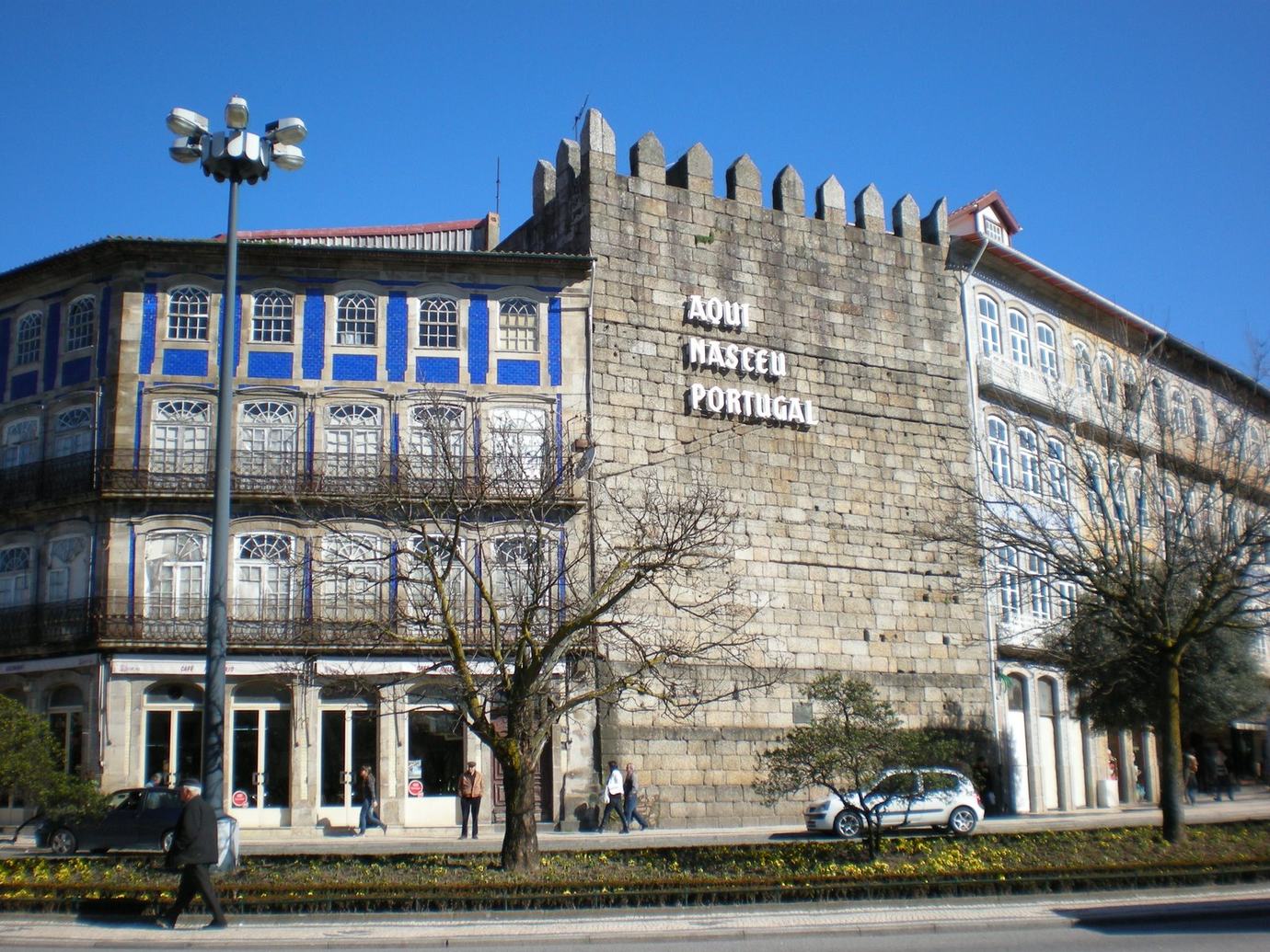 The granite Torre da Alfândega in Guimarães with the words Aqui Nasceu Portugal on its wall beside a blue-tiled townhouse