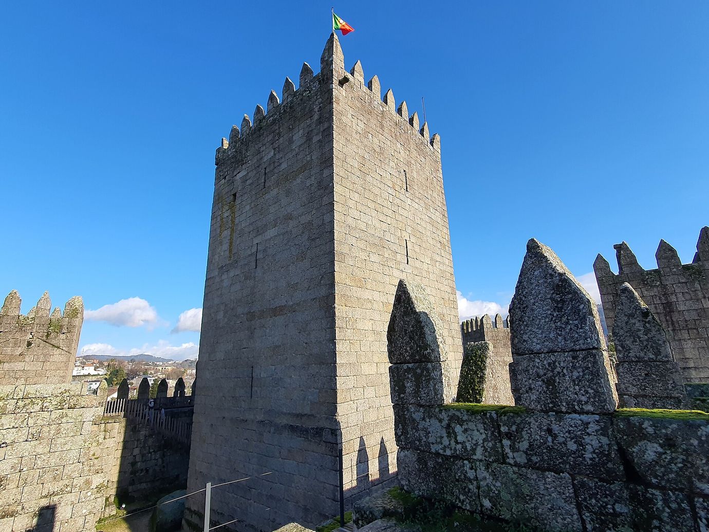 The granite keep of Guimarães Castle rising against a deep blue sky, with crenellated walls on either side