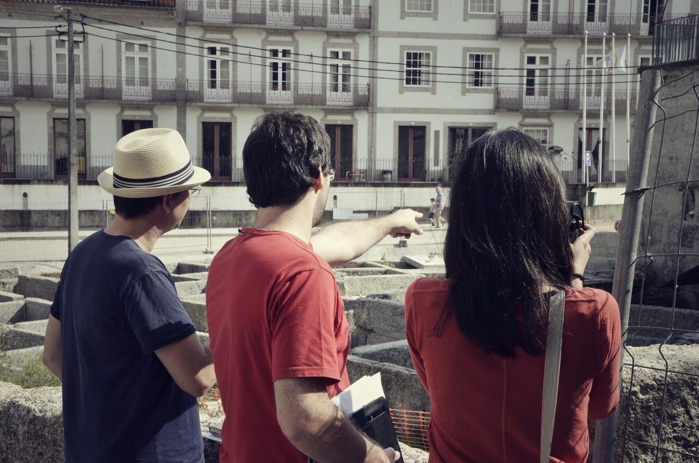 Three visitors looking down at the old stone tanning pools in the Couros district of Guimarães, with period buildings behind