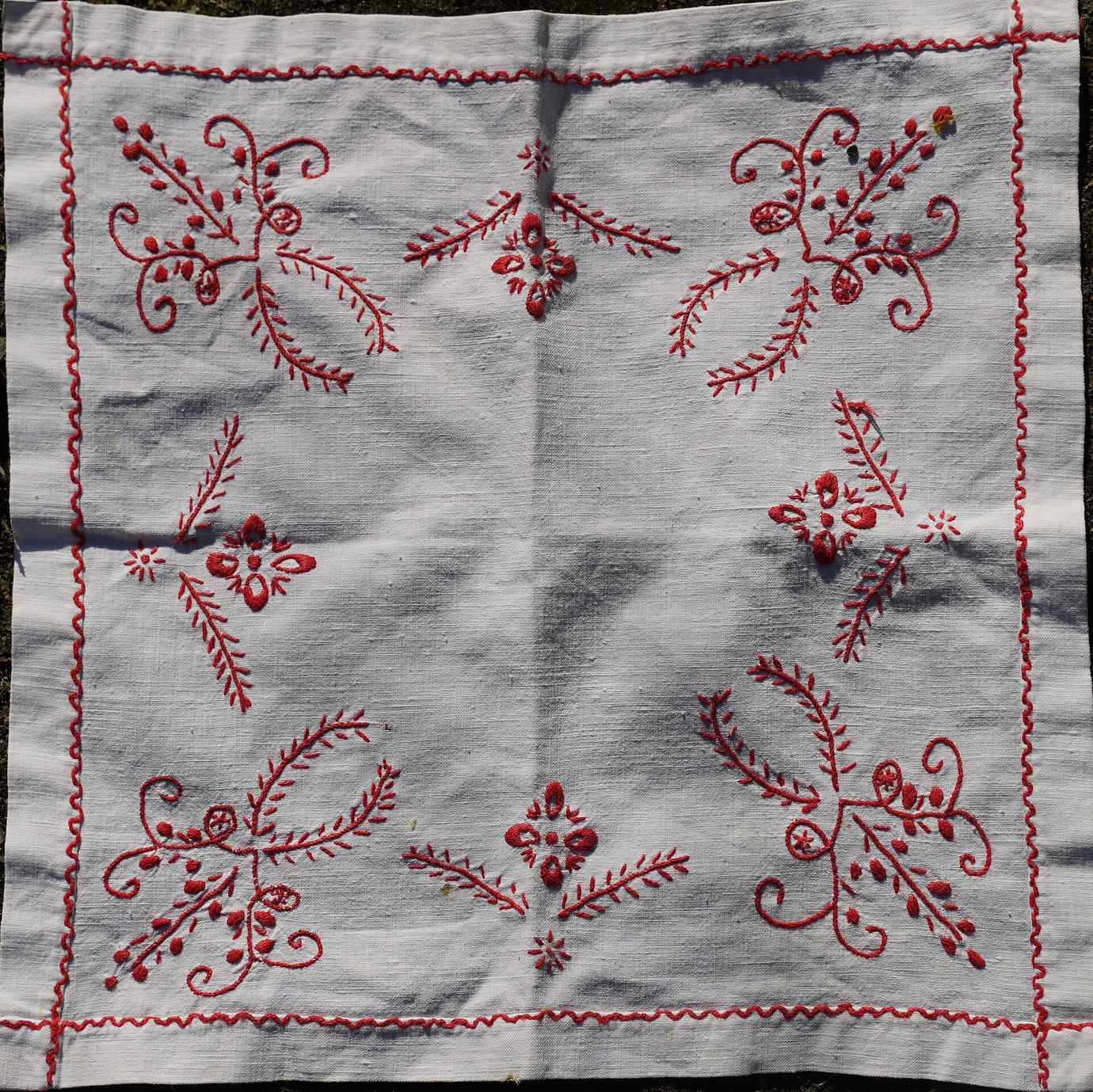 A square of grey linen with a red hand-embroidered floral border and motifs in the traditional Guimarães style