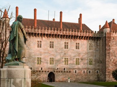 Guimaraes Hero Paco Duques The Palace of the Dukes of Braganza in Guimarães glowing in warm evening light, with the bronze statue of Afonso Henriques in the foreground