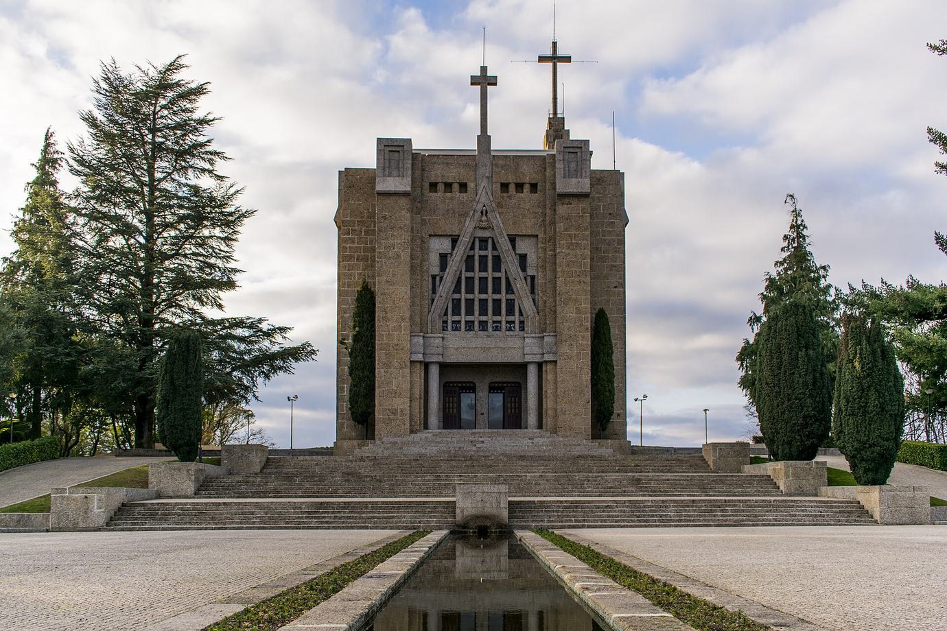 The granite Art Deco sanctuary of Penha with two crosses on its roof, set among cedars above a long reflecting channel