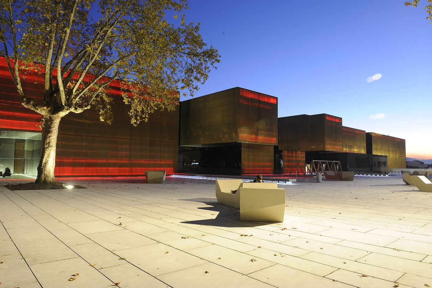 The dark gold and red box-shaped buildings of the Plataforma das Artes e da Criatividade in Guimarães at dusk