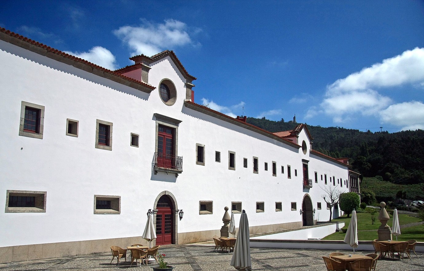The long white wall of the Monastery of Santa Marinha da Costa, now a pousada, with a terrace and wooded hills behind