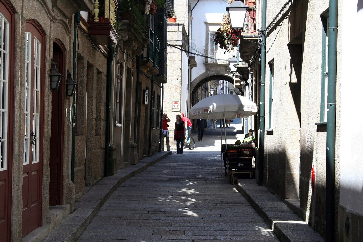 The narrow granite-paved Rua de Santa Maria in Guimarães, with an archway in the distance and a café umbrella in the sun