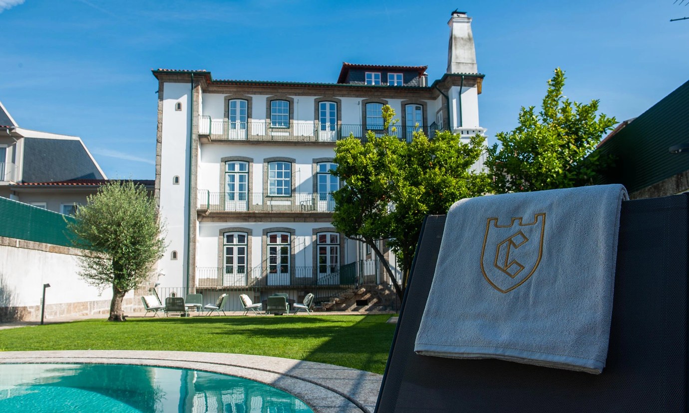 The white three-storey Torel Royal Court palace behind a garden and swimming pool under a clear blue sky in Guimarães