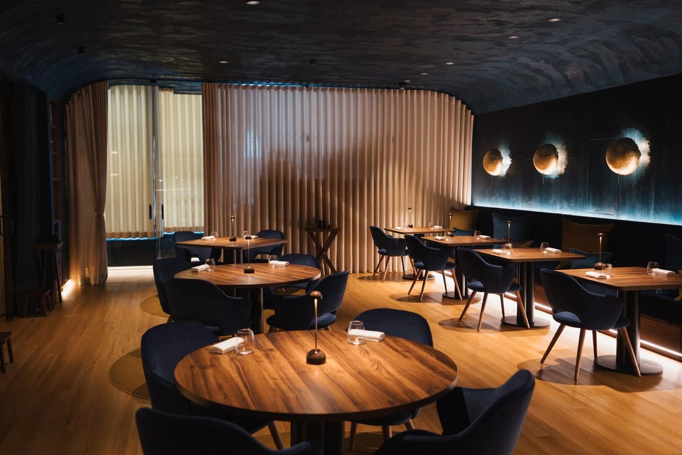 Dining room of the Henrique Sá Pessoa restaurant in Lisbon, with teal walls, round wall lights and a wooden slatted partition