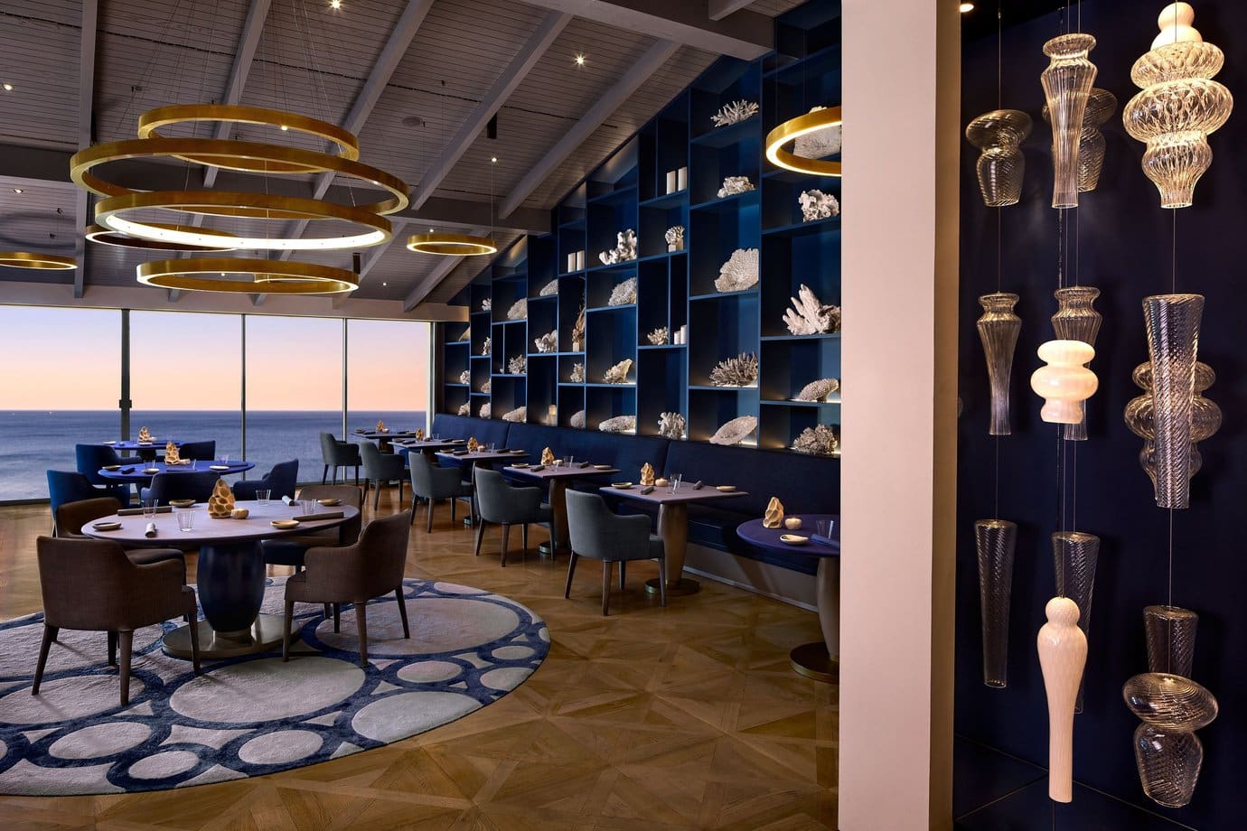 The deep blue Ocean dining room at Vila Vita Parc in Porches, with coral shelving, gold chandeliers and sea views at dusk